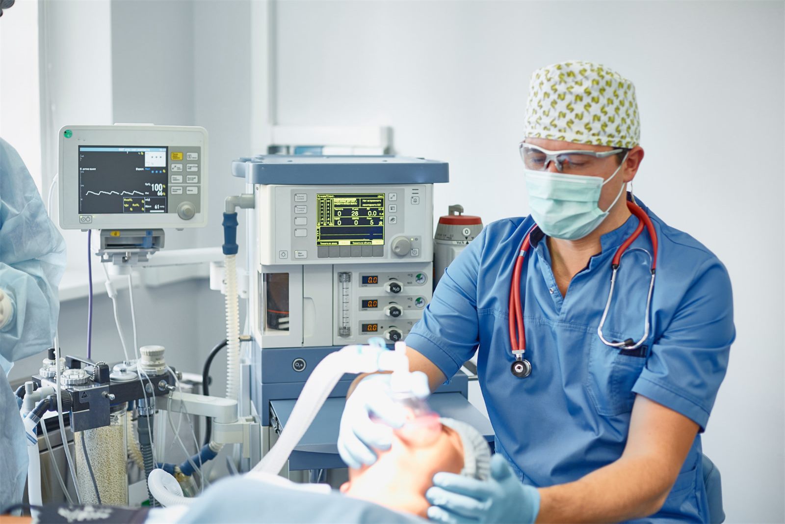 Anesthesia provider managing a patient's airway beside a full anesthesia machine
