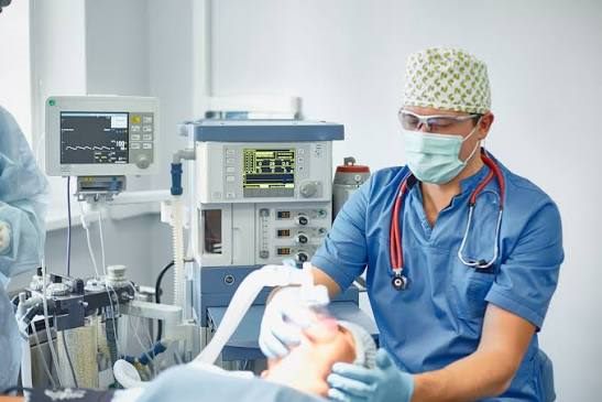 Anesthesia provider seated at the head of a patient with monitoring and anesthesia equipment