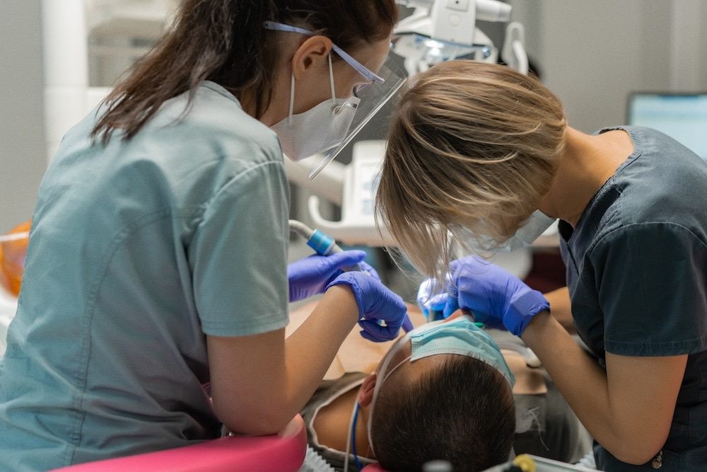 Two clinicians collaborating over a patient during a dental procedure