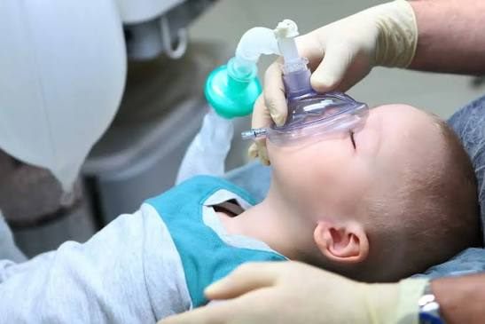 Anesthesia provider holding a small mask over a sleeping child before dental treatment